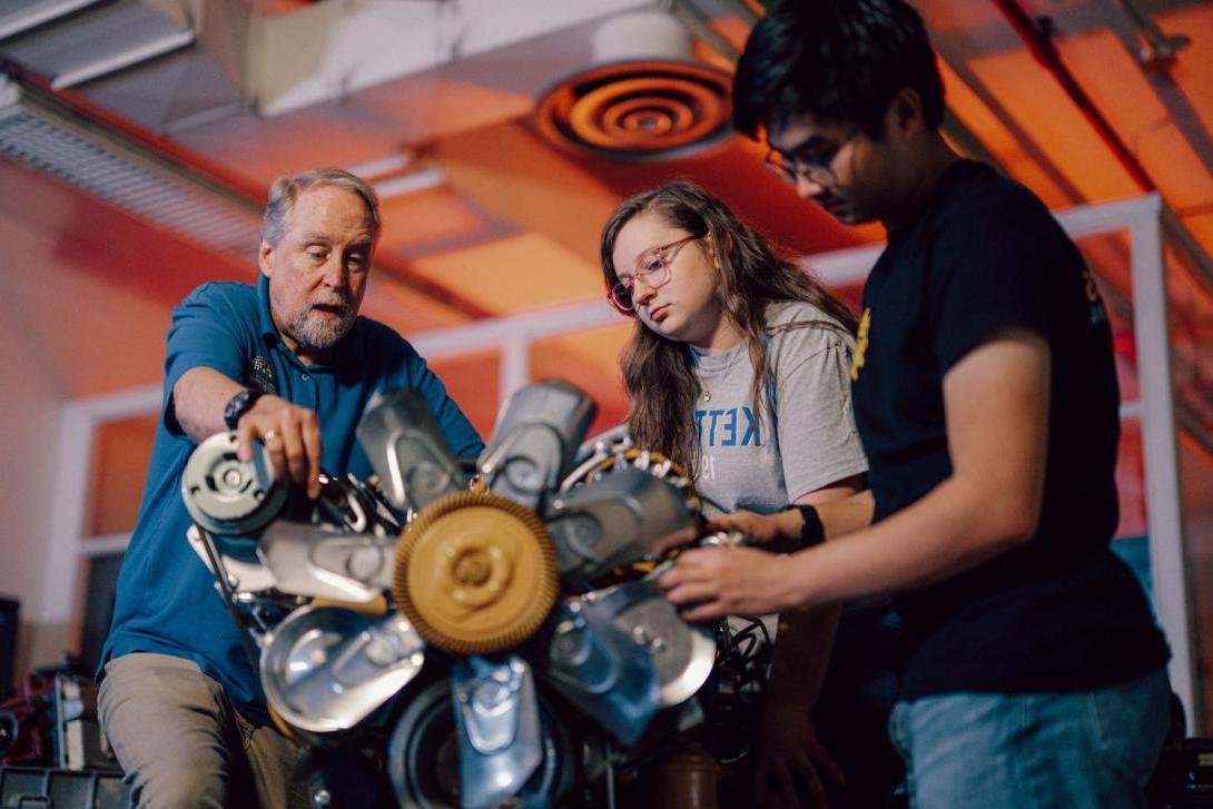 Two Kettering mechanical engineering students and a professor look closely at a car part in the Car Lab